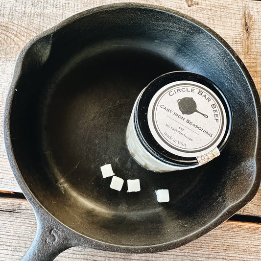 Black cast iron skillet with a can of seasoning on a wooden surface