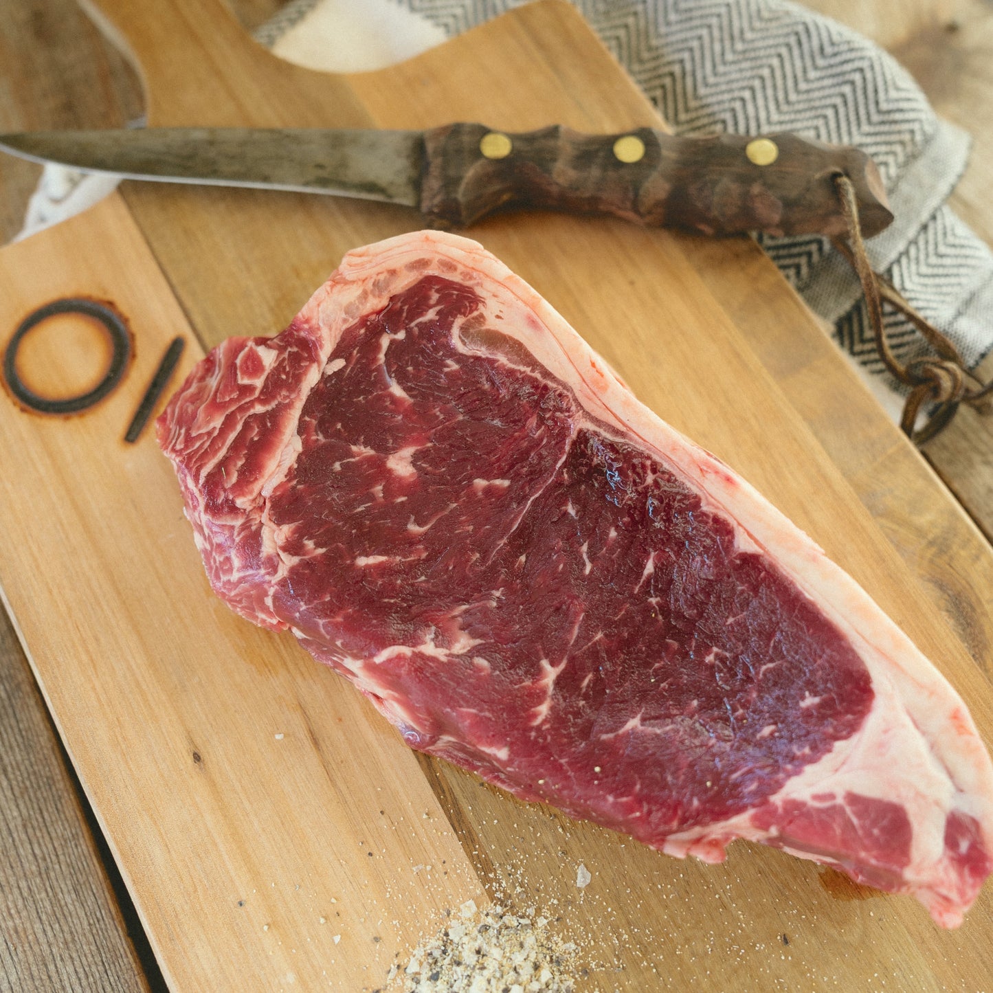 Raw steak on a wooden cutting board with a knife, on a rustic wooden surface.