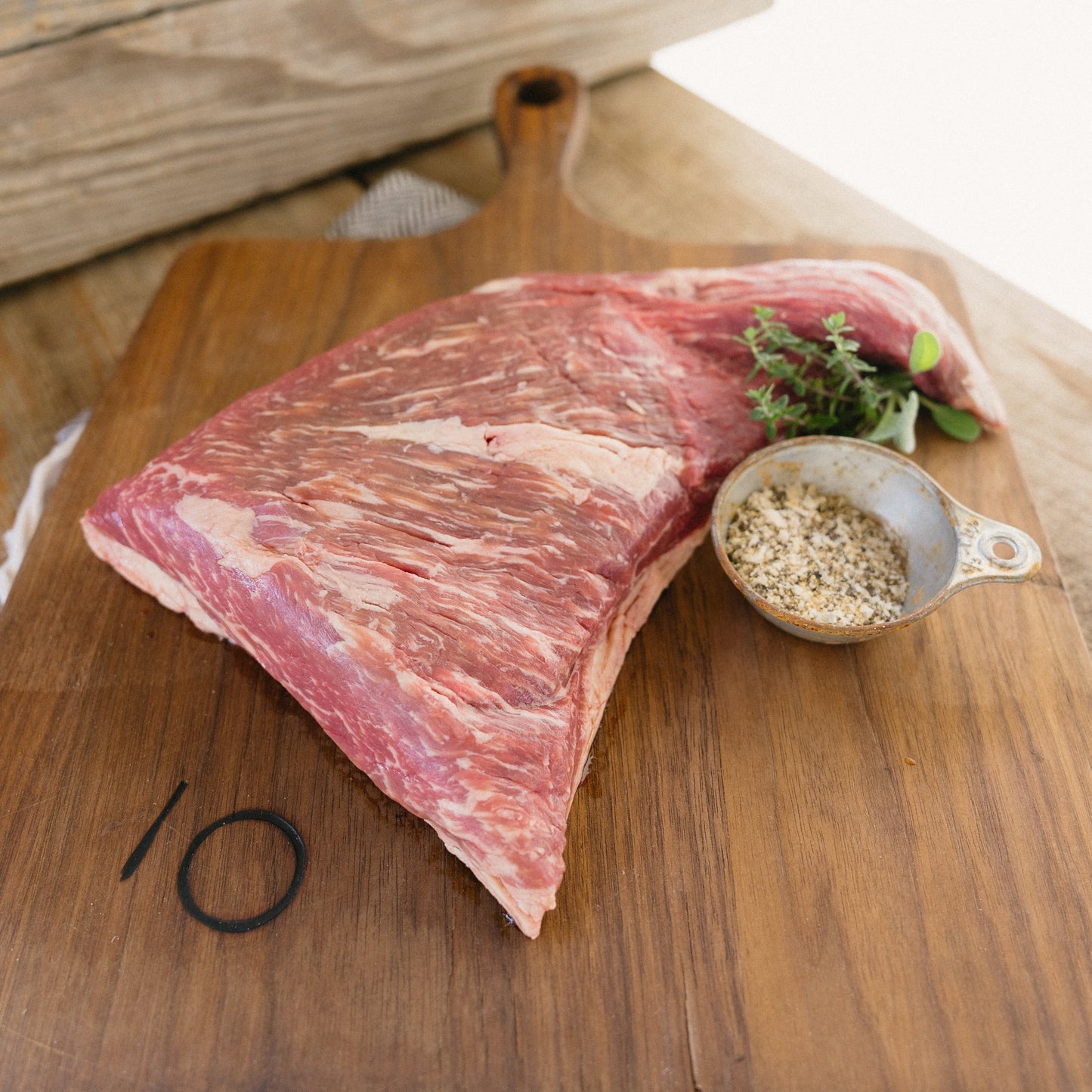 Raw meat on a wooden cutting board with a small bowl of seasoning.