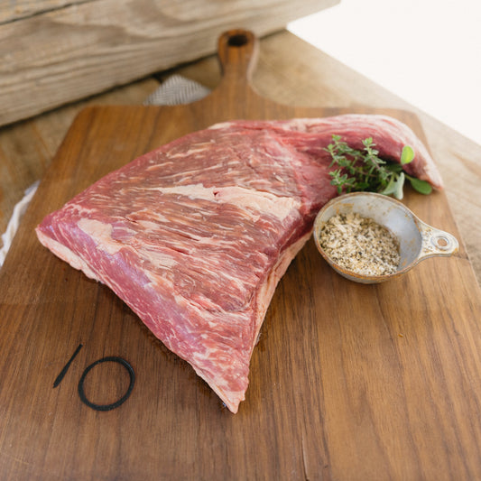 Raw meat on a wooden cutting board with a small bowl of seasoning.
