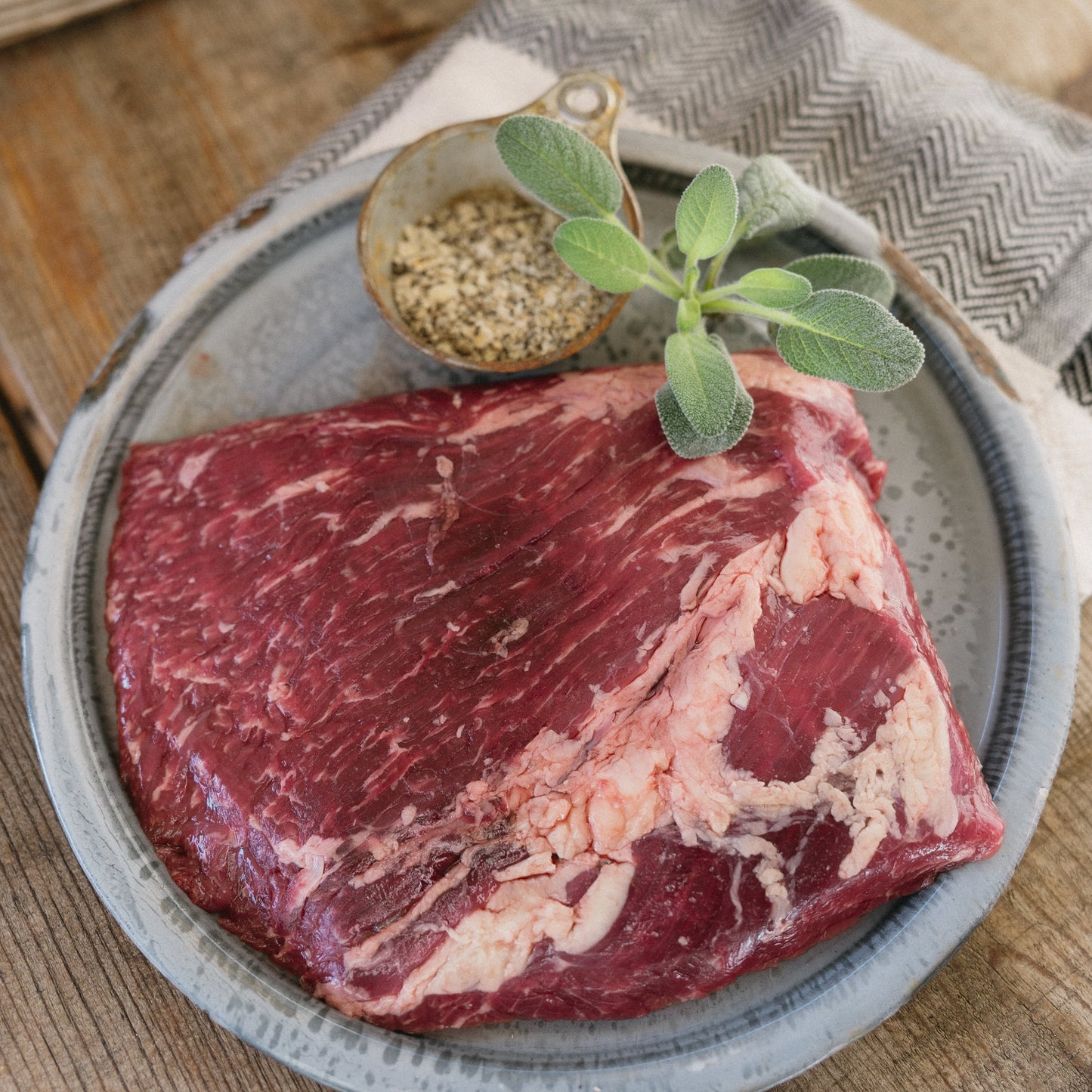 Raw steak on a plate with herbs and spices on a wooden surface