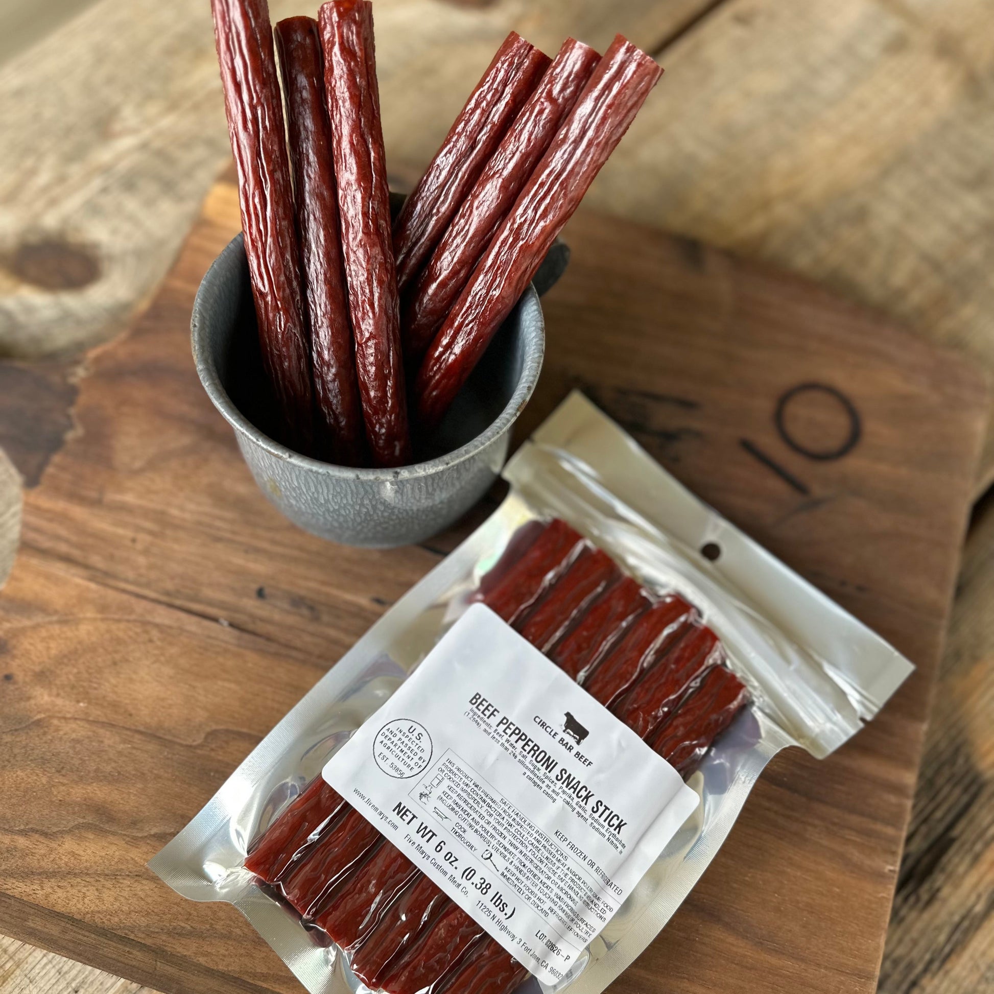 Packaged beef jerky sticks on a wooden surface with a small bowl of jerky sticks.