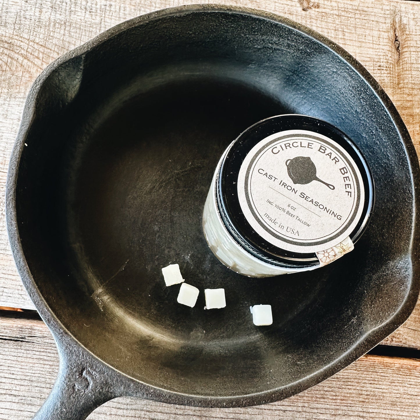 Black cast iron skillet with a can of seasoning on a wooden surface