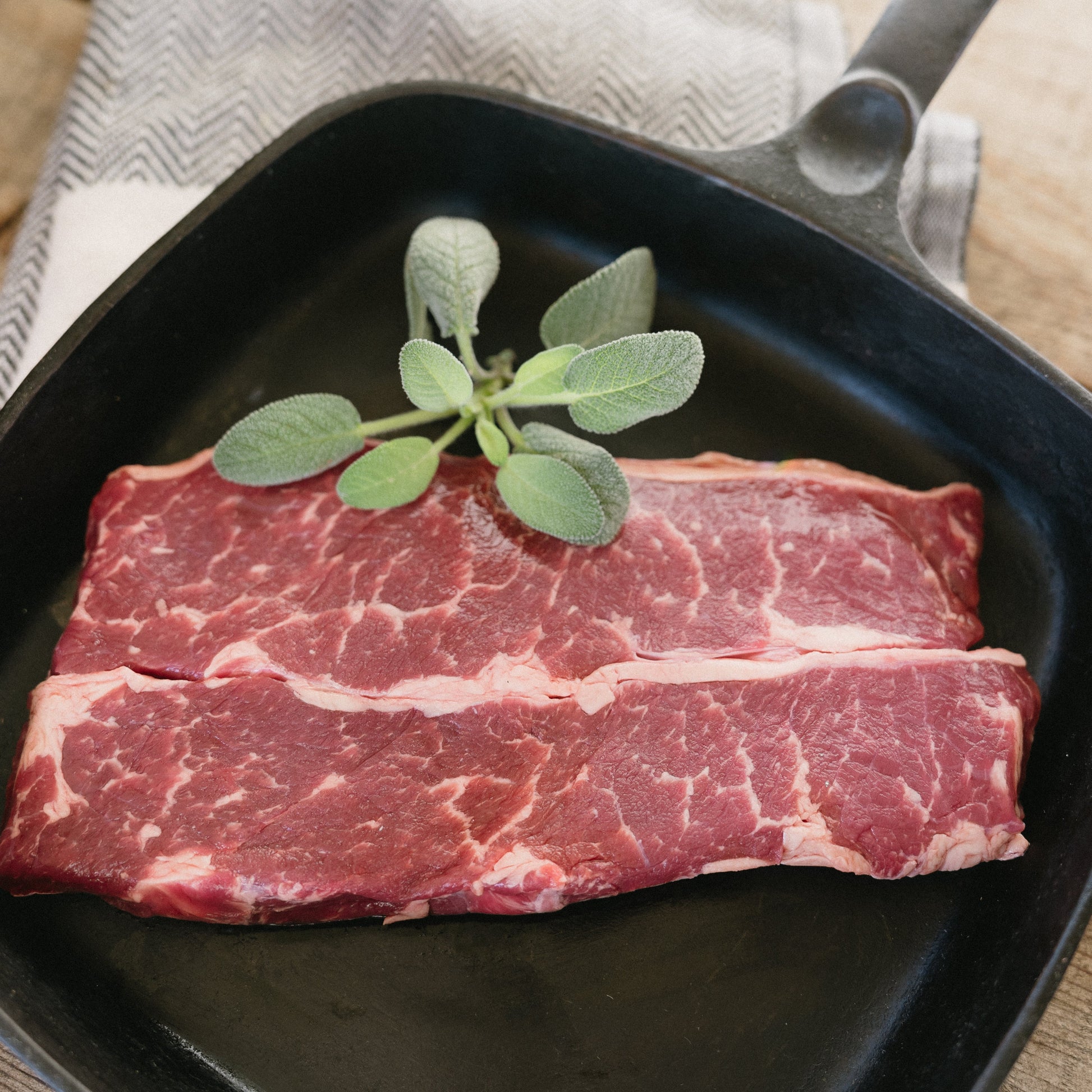 Raw beef steaks with sage leaves in a black skillet on a wooden surface