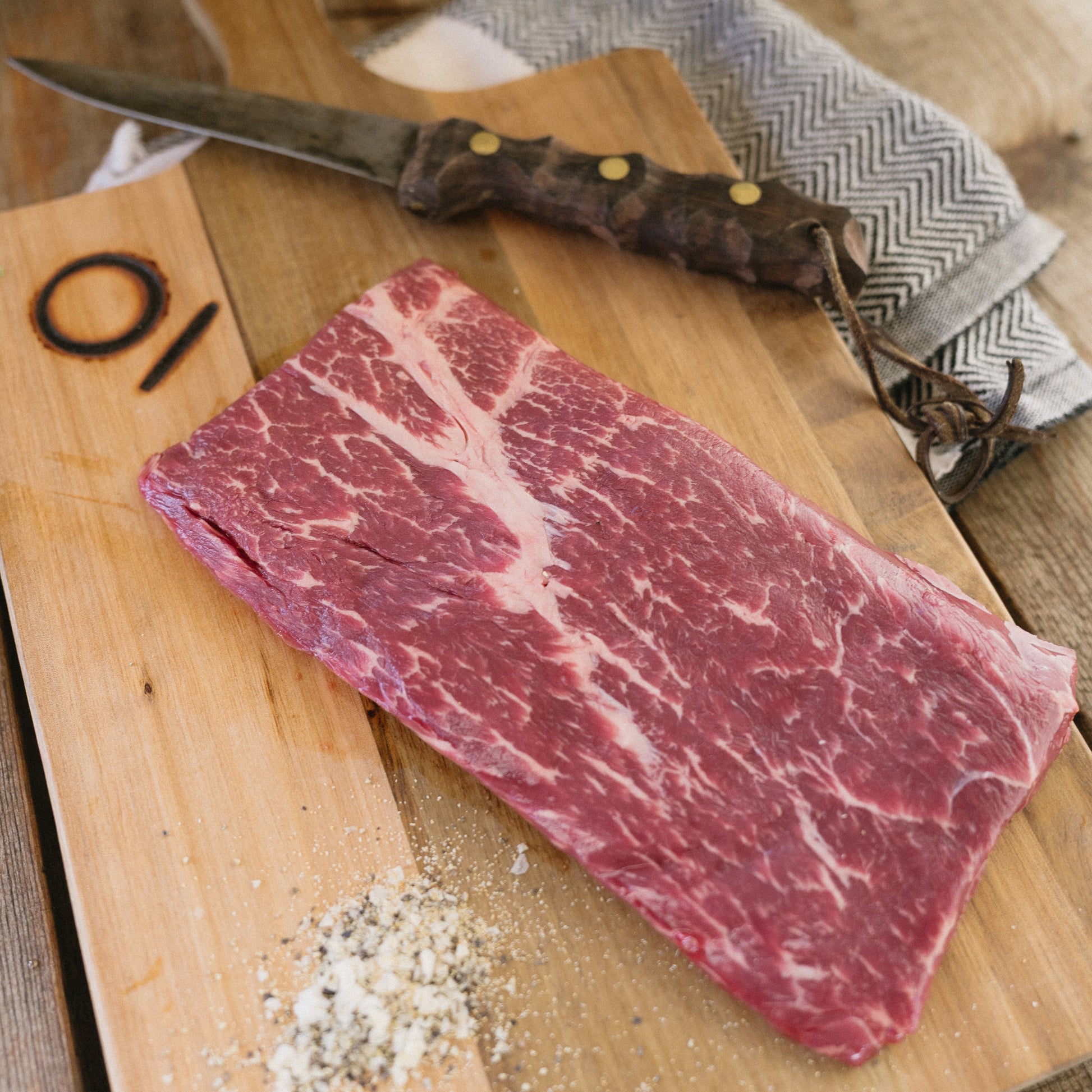Raw steak on a wooden cutting board with a knife and salt, on a rustic wooden surface.