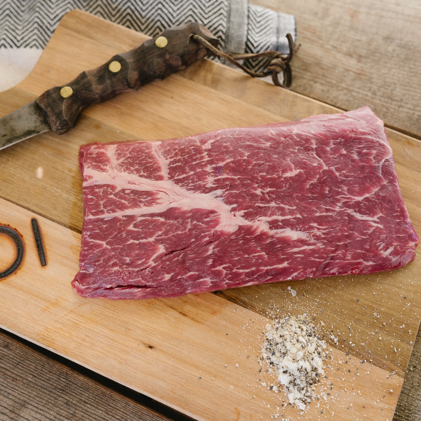 Raw steak on a wooden cutting board with a knife and seasoning.