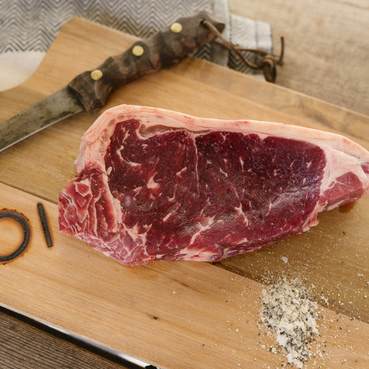 Raw steak on a wooden cutting board with a knife and seasoning.