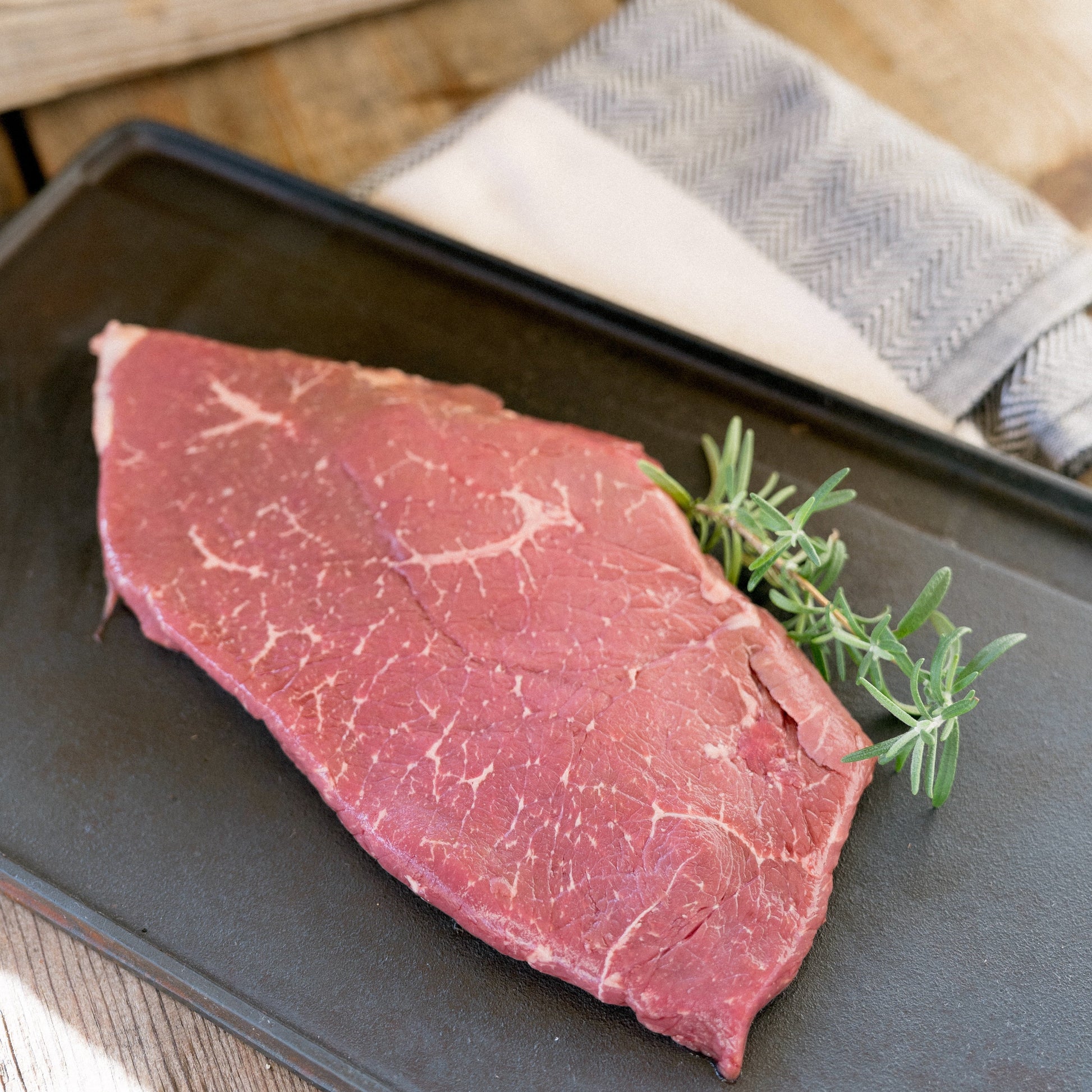 Raw steak with rosemary on a black tray outdoors