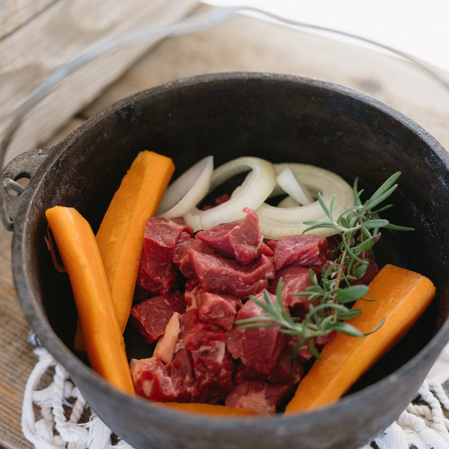 Cast iron pot with beef, carrots, and onions on a wooden surface