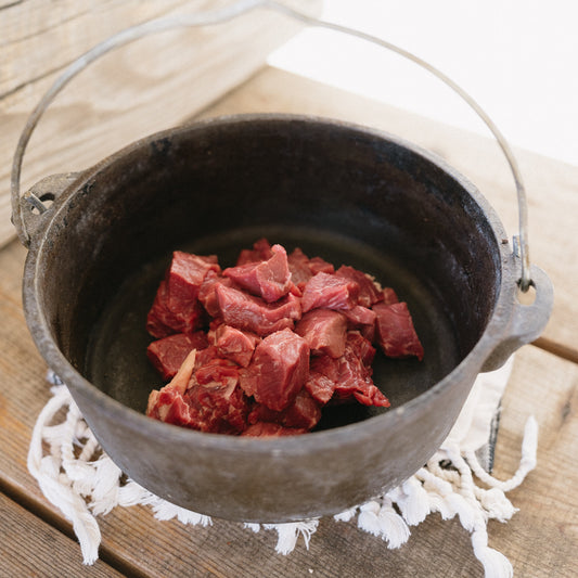 Dutch oven with raw beef on a wooden surface